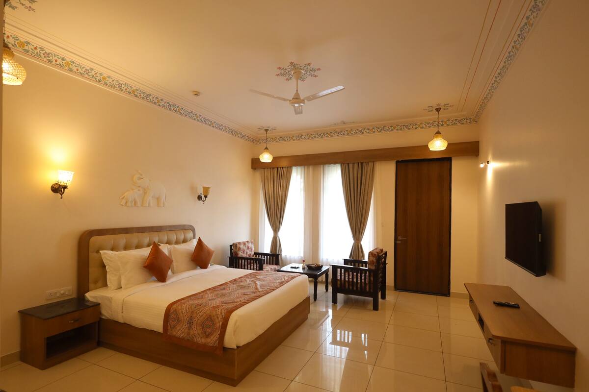 A hotel room with a large bed, a desk, a chair, a television, and a ceiling fan.