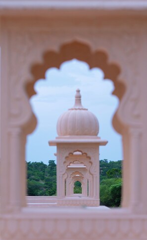 A view through an ornate archway of a temple with a dome and a gateway, set against a backdrop of lush greenery. - Trulyy The Shakti Vilas (Udaipur)