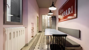 Un couloir étroit avec un radiateur, une table entourée de chaises, des lampes suspendues et un panneau sur le mur.