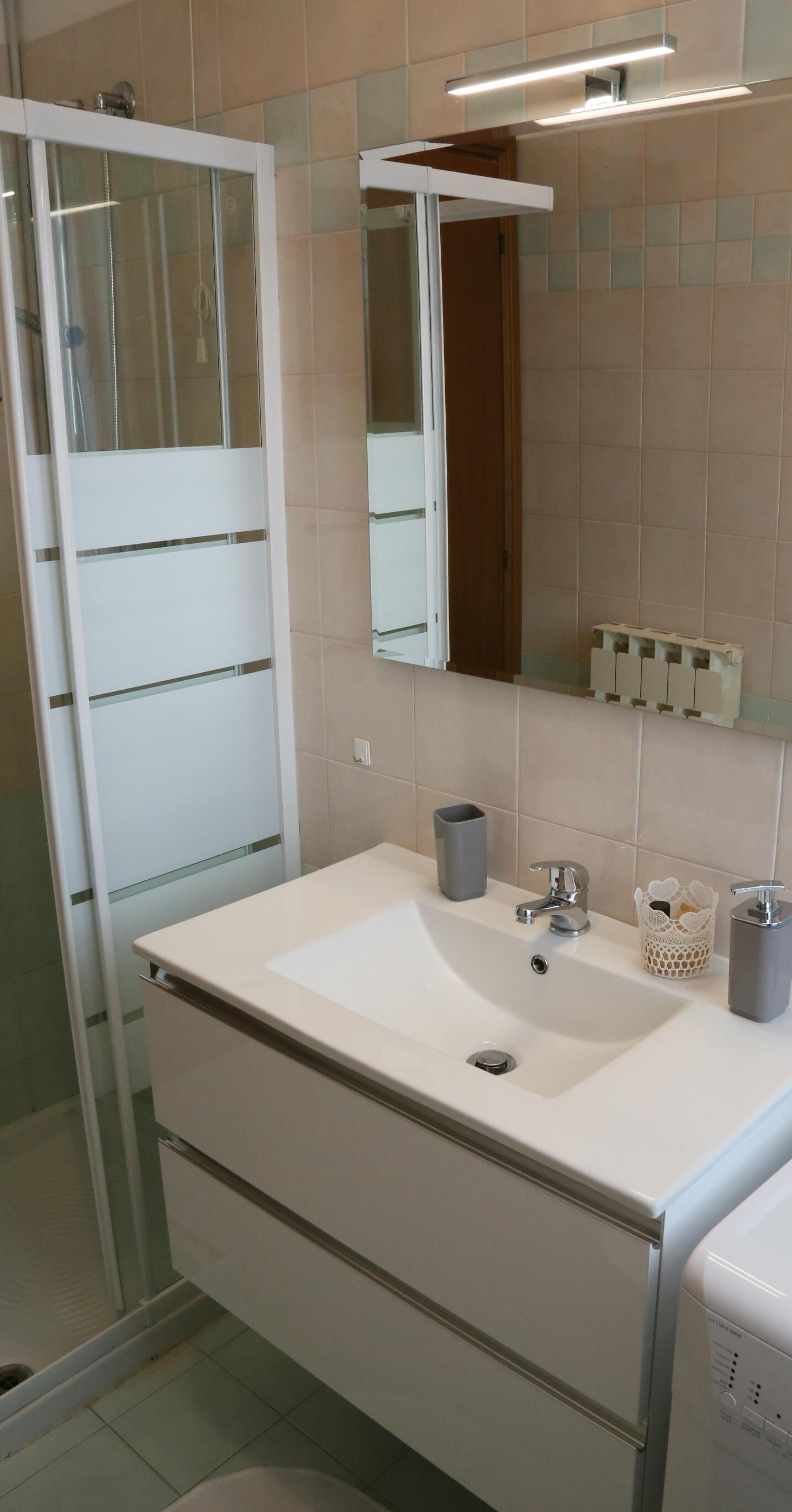 Un baño con lavamanos blanco, espejo, cabina de ducha y retrete.