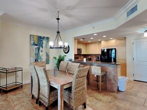A dining area with wicker chairs, a wooden table, and a chandelier.