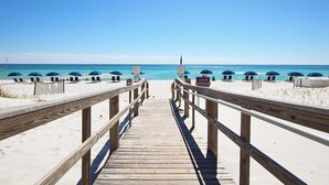 A wooden boardwalk leading to a beach with umbrellas and lounge chairs.