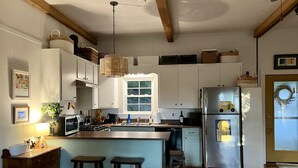 Eine Küche mit Holzbalken, weißen Schränken, einem Edelstahlkühlschrank und einem Fenster mit Blick auf Grünflächen.