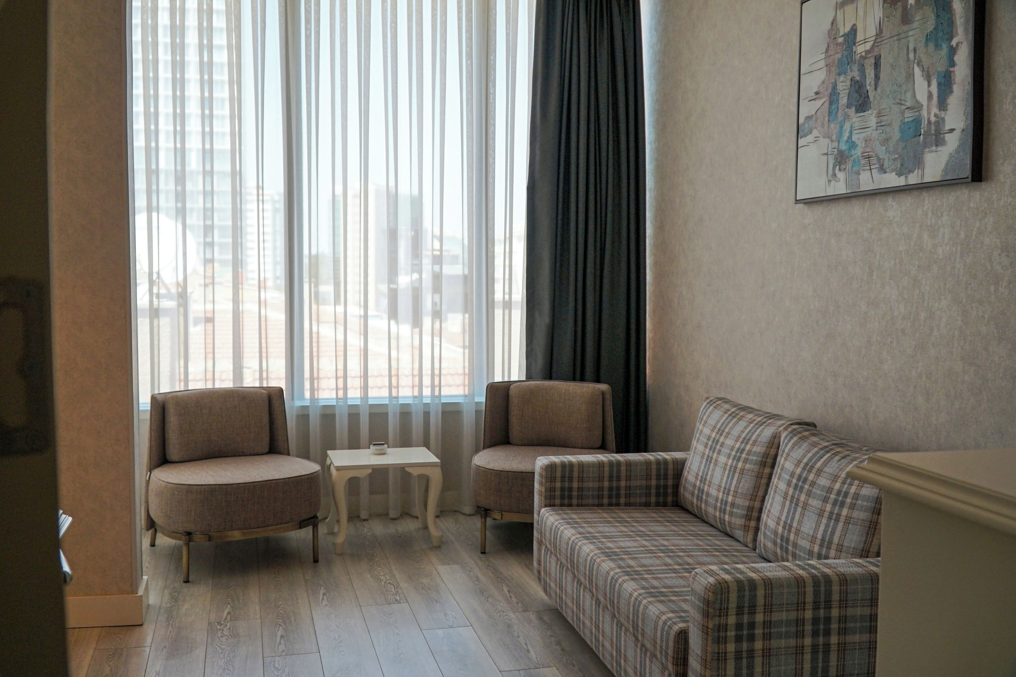 A room with a sofa, two armchairs, a small table, and a large window with curtains.
