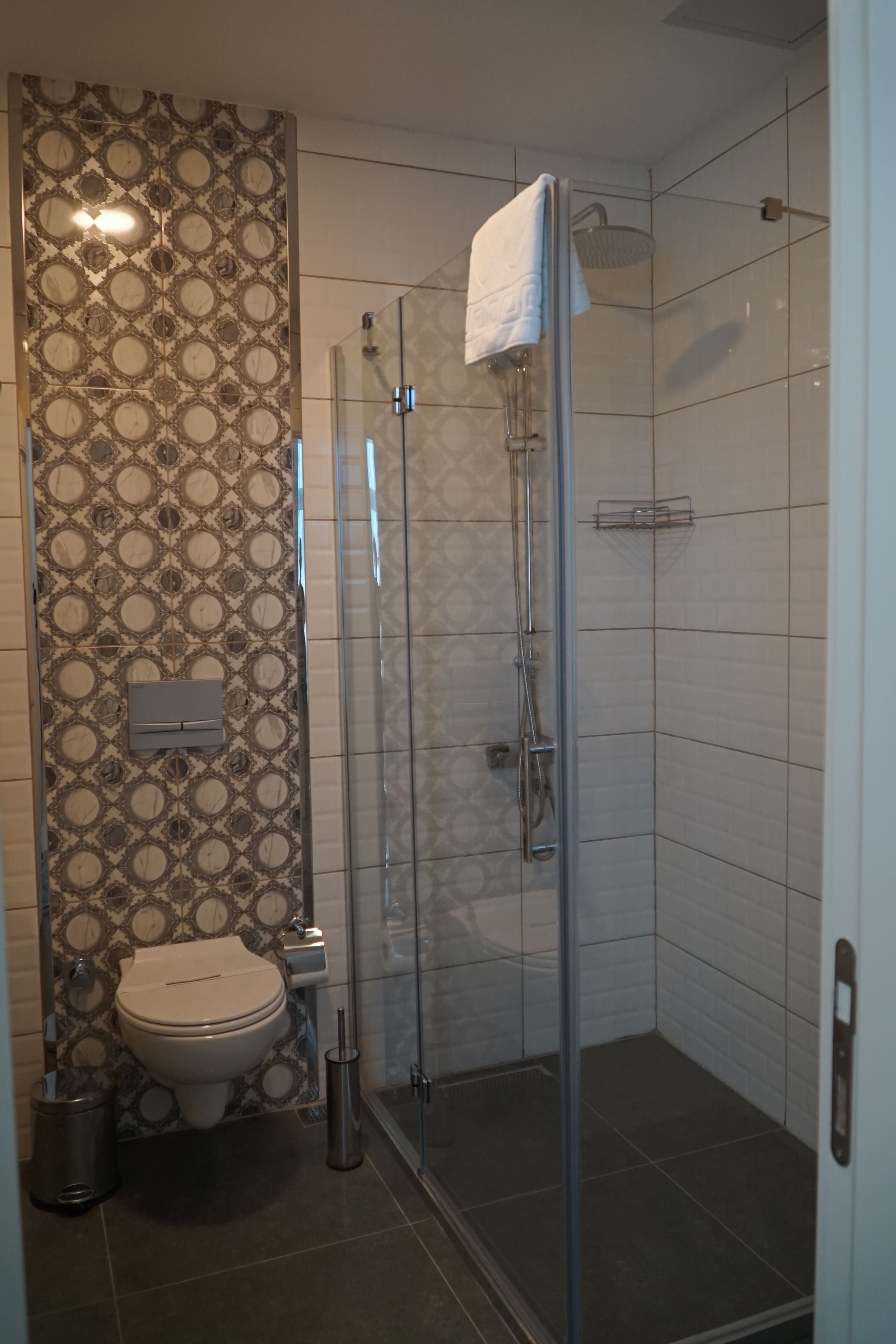 Casa de banho com sanita, chuveiro com porta de vidro e azulejos estampados.