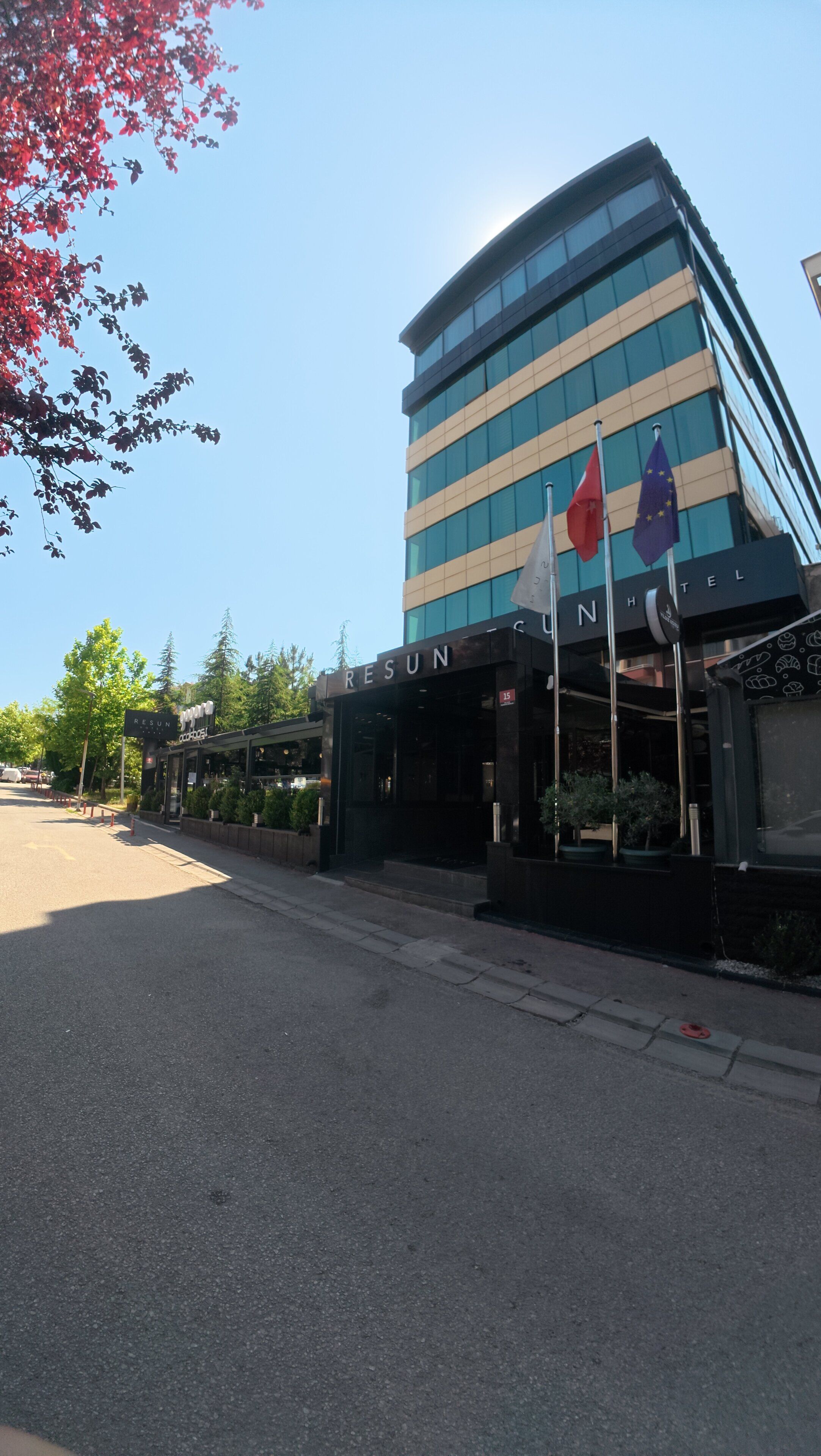 A modern hotel building with a sign reading 'RESUN HOTEL' and flags of the European Union and another country.