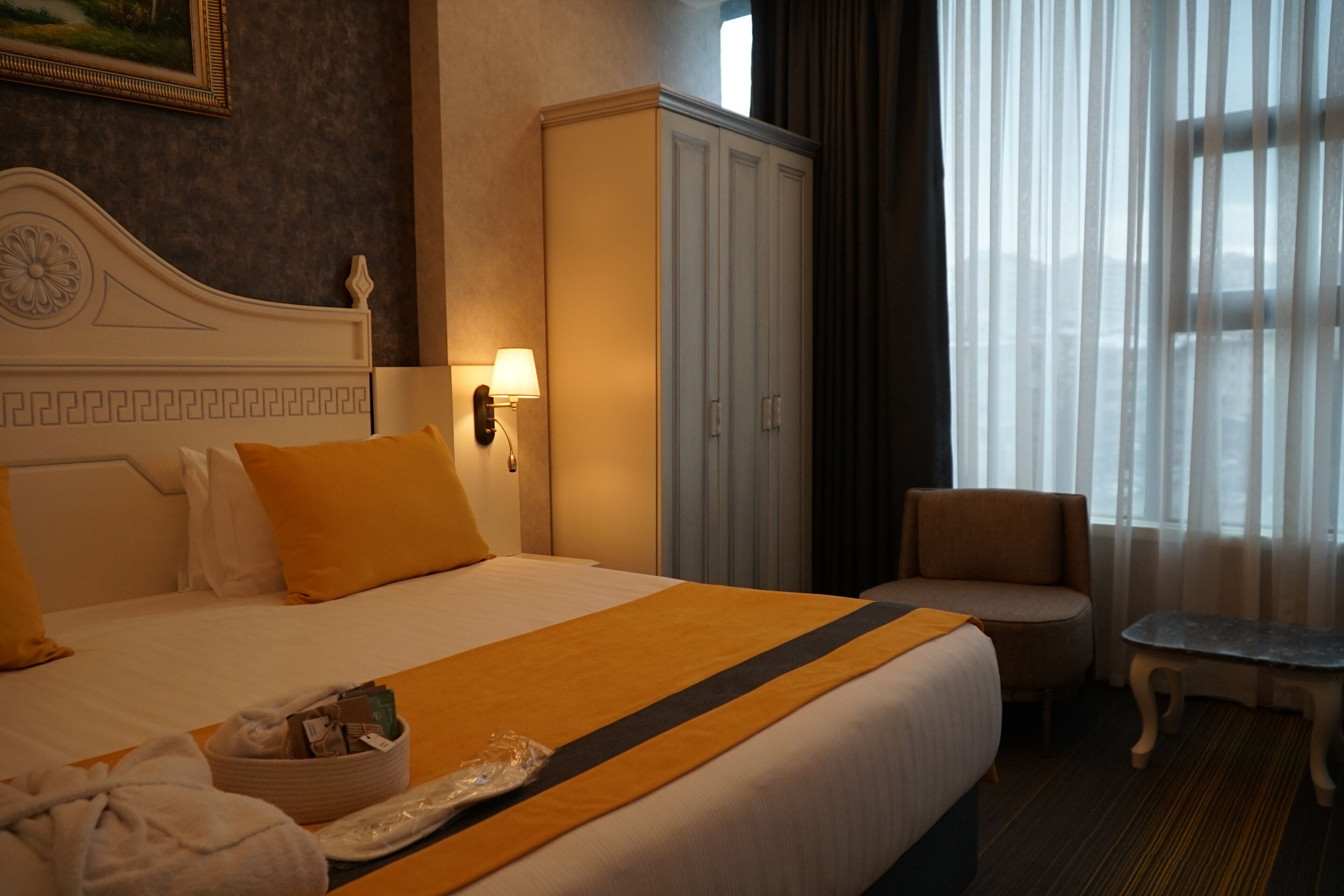 A hotel room with a large bed, a wardrobe, a chair, and a small table.