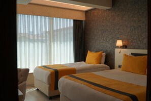 Une chambre d’hôtel avec deux lits, une grande fenêtre avec des stores, une lampe et une chaise.