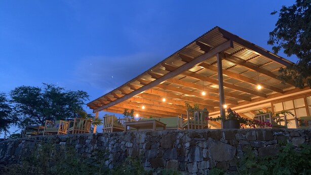 A modern building with a stone retaining wall, wooden deck, and outdoor seating area. - La Fora Ecolodge (São Filipe)