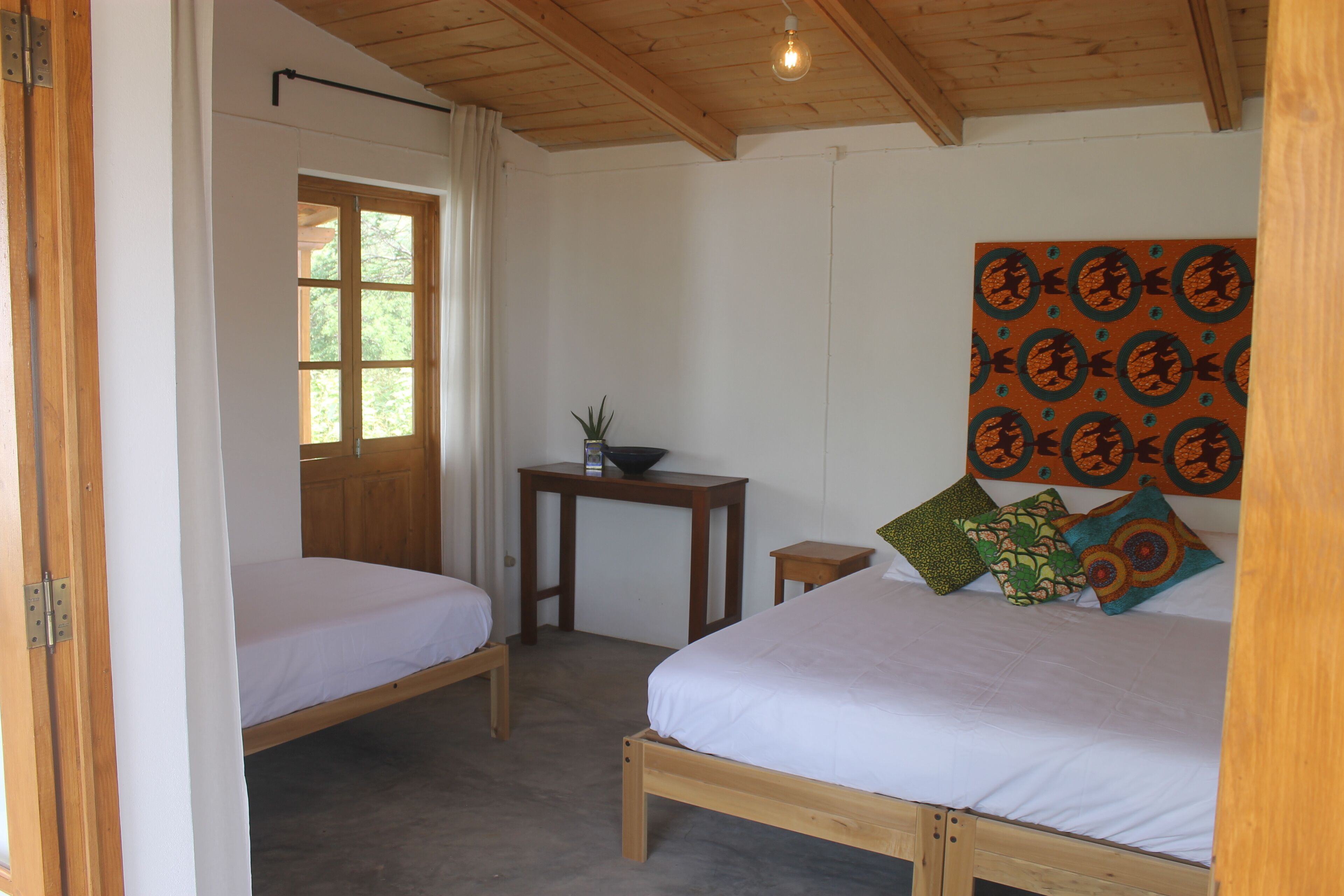 A bedroom with two wooden beds, a small table with a bowl, and a wall with a patterned tapestry.