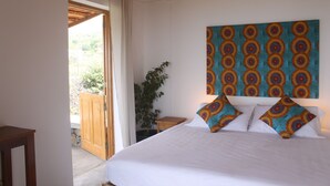 A bedroom with a bed, a wooden headboard, a nightstand, a potted plant, and a view of the outside. - La Fora Ecolodge (São Filipe)