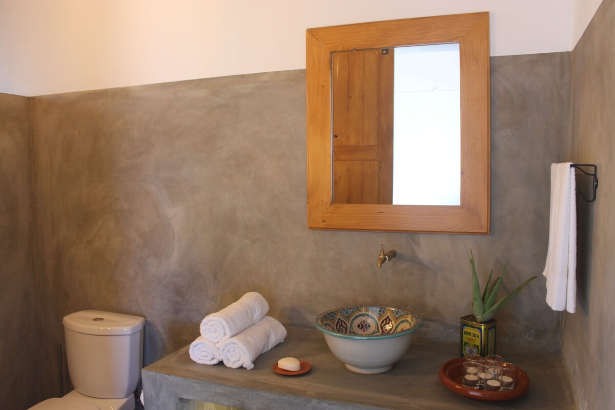 A bathroom with a toilet, a sink with decorative bowls, a mirror, and a towel rack.