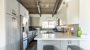 Une cuisine moderne avec des meubles blancs, des appareils en acier inoxydable et un îlot central doté de tabourets.