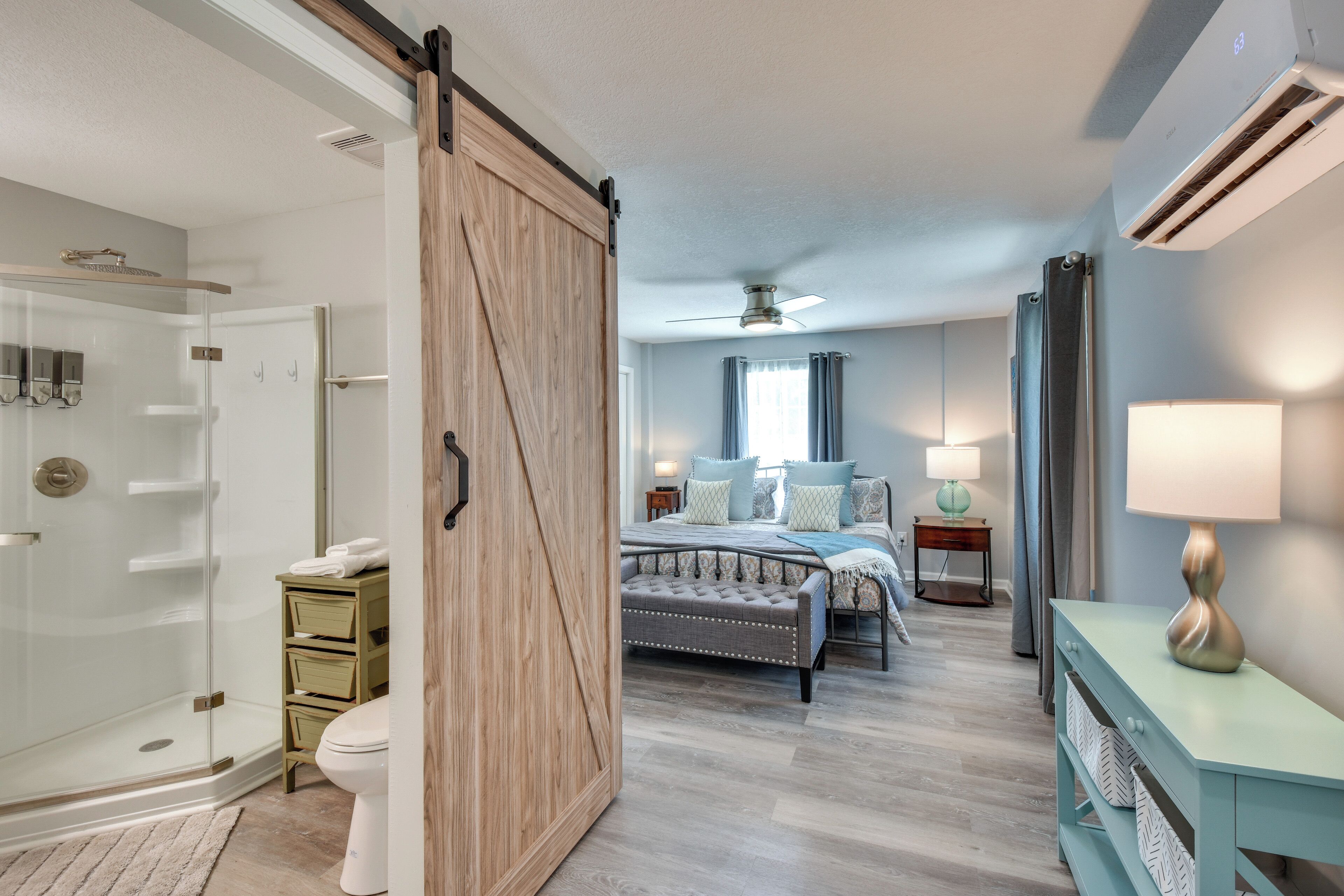 A modern bedroom with a sliding door, a bed with a tufted headboard, a bedside table, a lamp, and a nightstand.