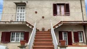 A two-story building with a central staircase, potted plants, and a white car parked in front. - Holiday home with panoramic terrace ideal for families and couples (Cortona)