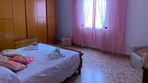 Ein Schlafzimmer mit Bett, Kleiderschrank, Stuhl und einem Fenster mit Vorhängen.