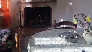 Ein Essbereich mit einem runden Tisch, der mit einer Spitzentuchbedeckung versehen ist, einer Kristallleuchtreiter und einem Kamin im Hintergrund.