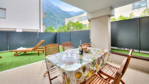 A patio with a table set for two, chairs, a bottle of champagne, and a fruit basket. - Casa Karin With Large Terrace and Garden (Riva del Garda)