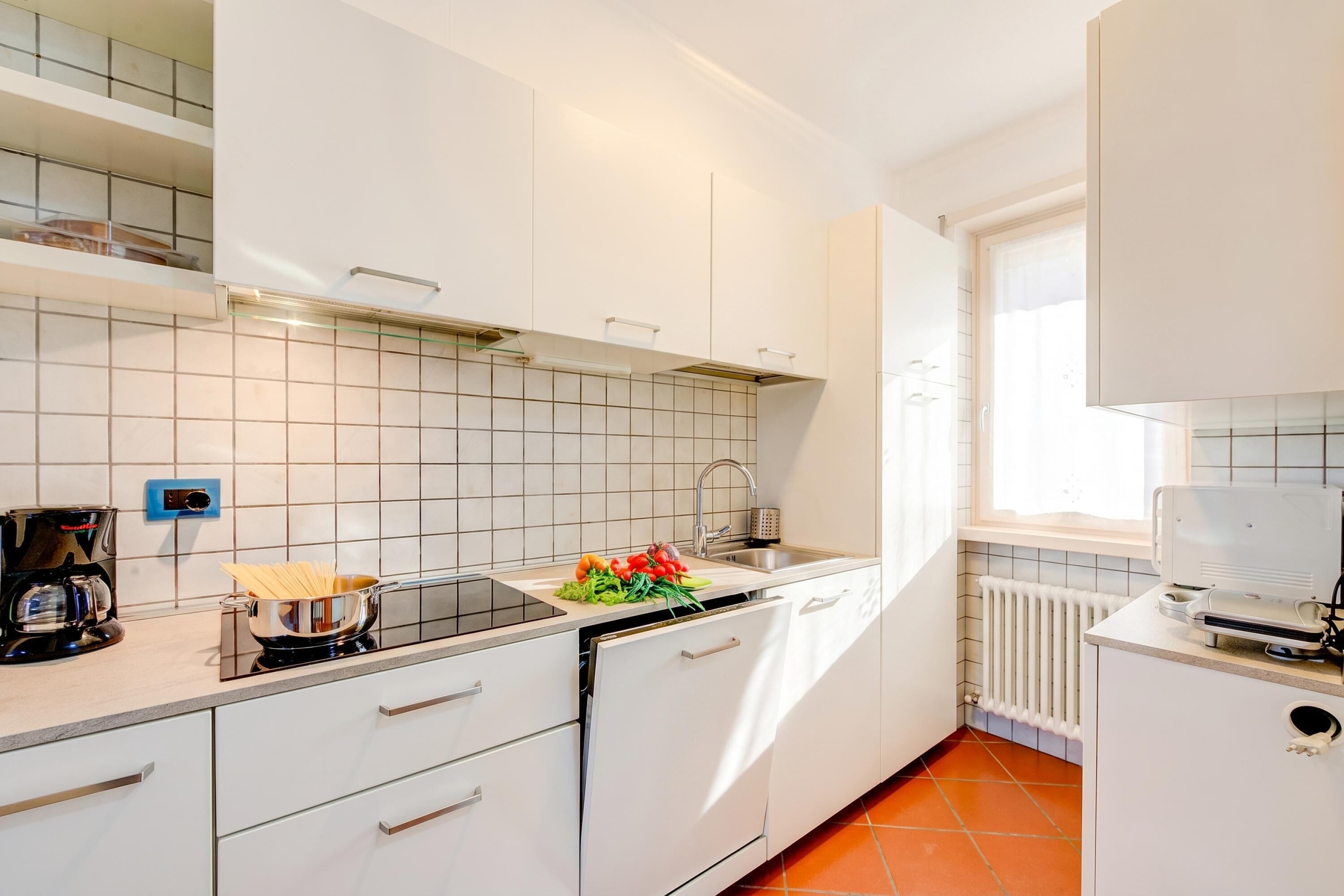 Une cuisine moderne avec des meubles blancs, une cuisinière, un évier et une fenêtre.