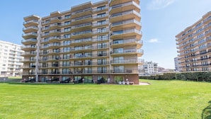 A multi-story residential building with balconies, a grassy courtyard, and a clear sky. - Westhinder 200m From Sea (De Panne)
