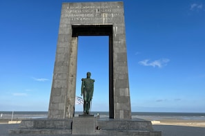 A monument with a statue, a clear sky, and a beach in the background.