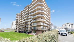 A multi-story residential building with balconies, a paved driveway, and a well-maintained lawn. - Westhinder 200m From Sea (De Panne)