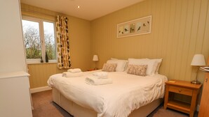 A neatly made bed with white linens and towels, a bedside table with a lamp, and a window with curtains. - Oak Lodge (Preston)