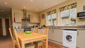A compact kitchen with a dining table, chairs, a washing machine, and a clock on the wall. - Oak Lodge (Preston)