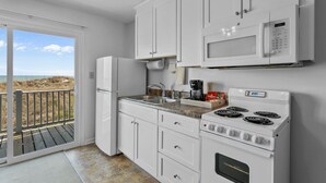 A kitchen with white cabinets, a microwave, a stove, and a sink. - The Beach House (Carolina Beach)