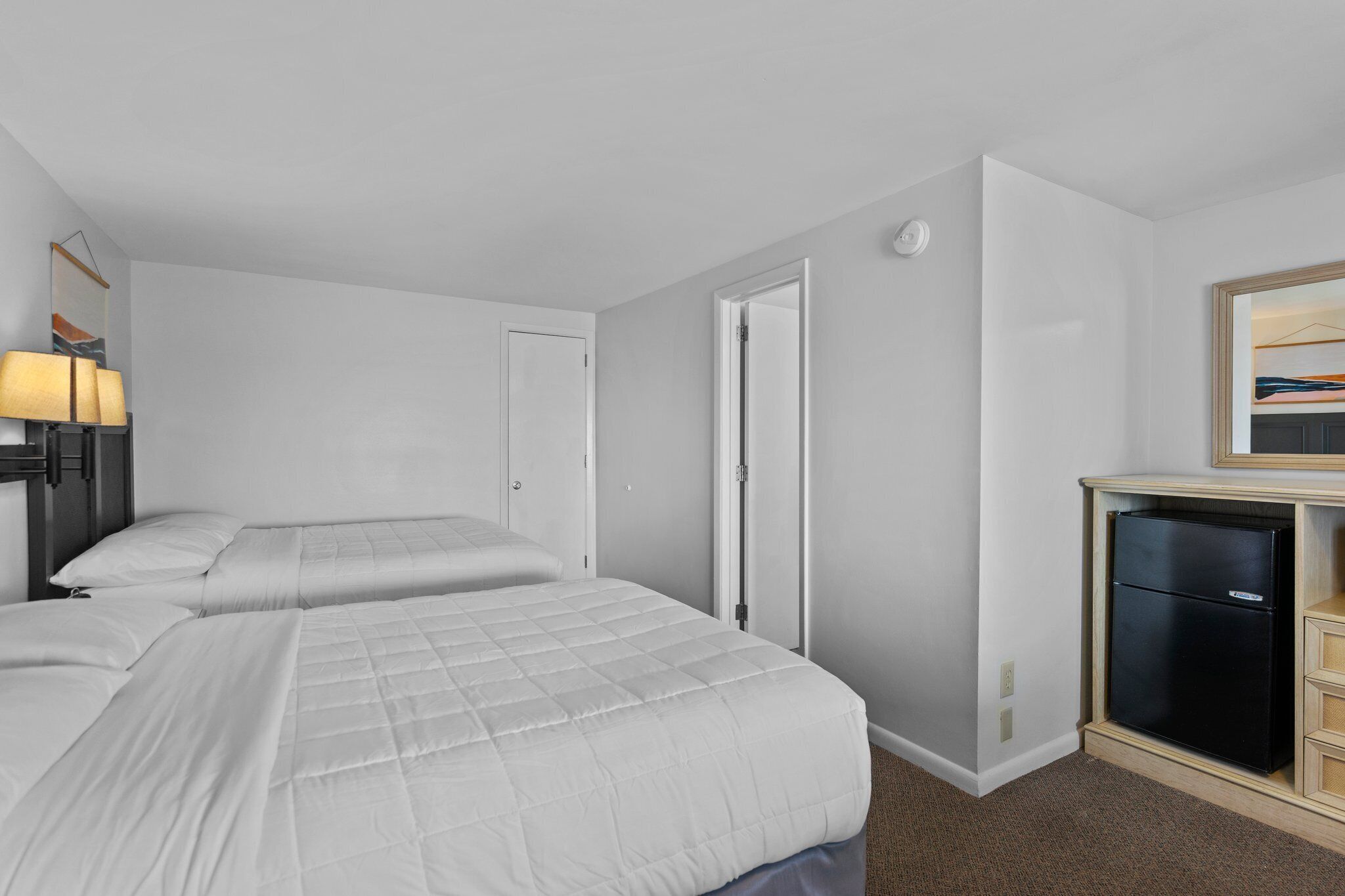 Une chambre d’hôtel avec deux lits, un bureau doté d’un réfrigérateur et une lampe fixée au mur.