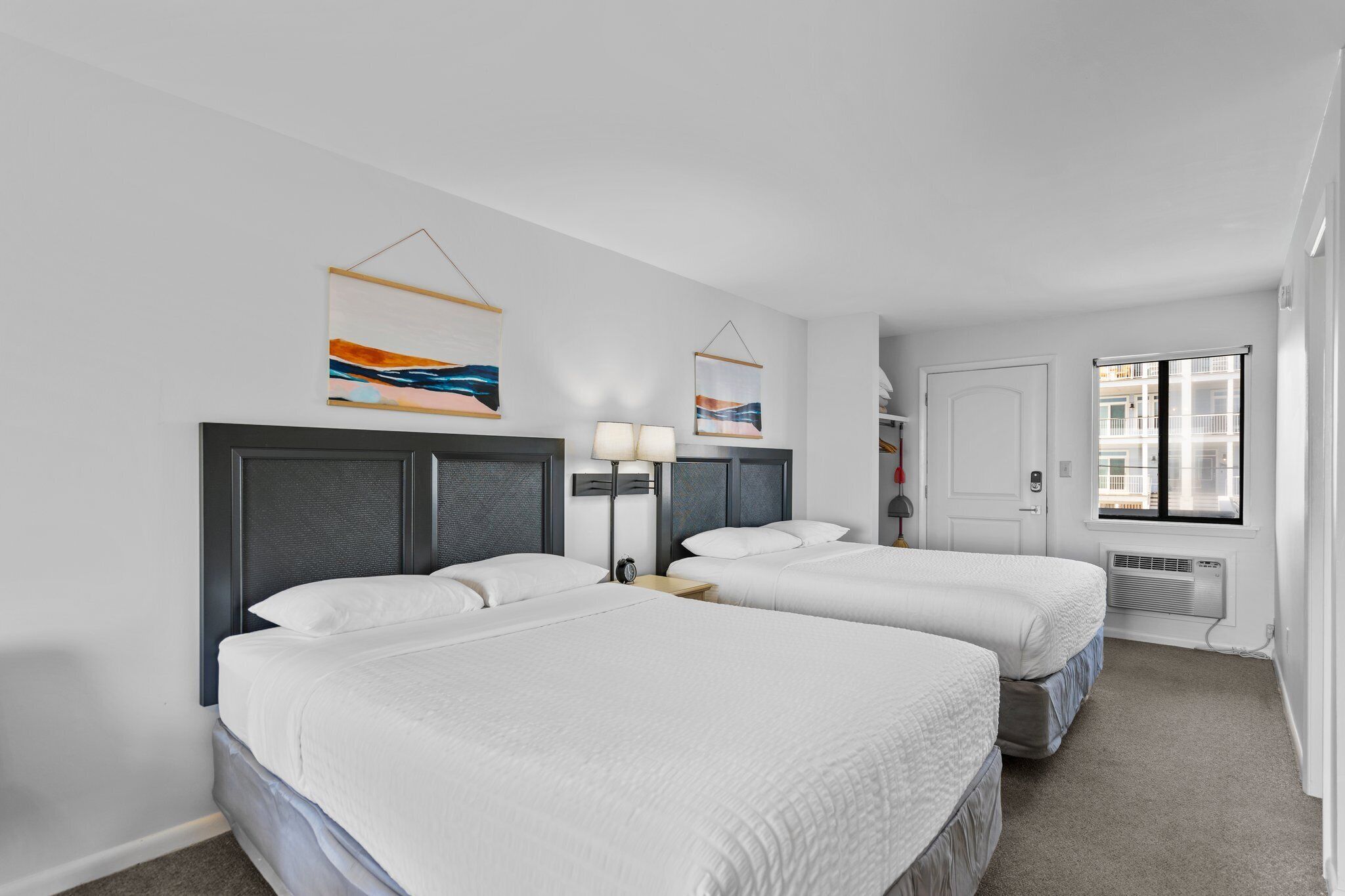 A hotel room with two beds, a window, and artwork on the walls.