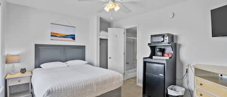 Habitación de hotel con cama, mesita de noche, escritorio, cubo de basura, microondas, televisión y ventilador de techo.