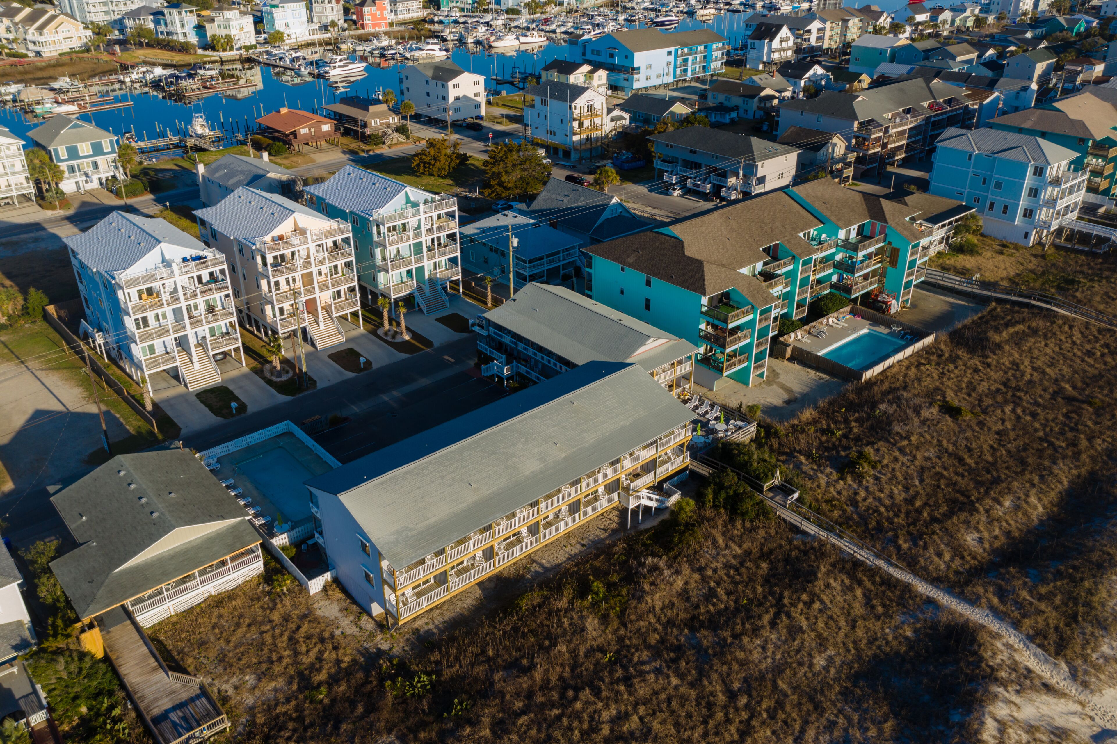 Vista aérea de una zona residencial costera con varios edificios de varios pisos, un puerto deportivo y una gran piscina.