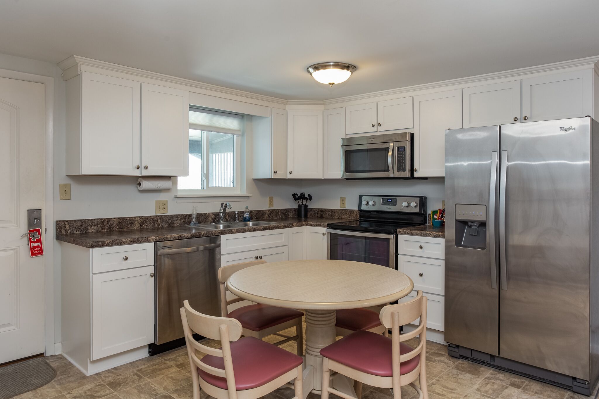 A modern kitchen with white cabinets, stainless steel appliances, a granite countertop, and a round dining table with chairs.