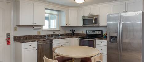 A modern kitchen with white cabinets, stainless steel appliances, a granite countertop, and a round dining table with chairs.