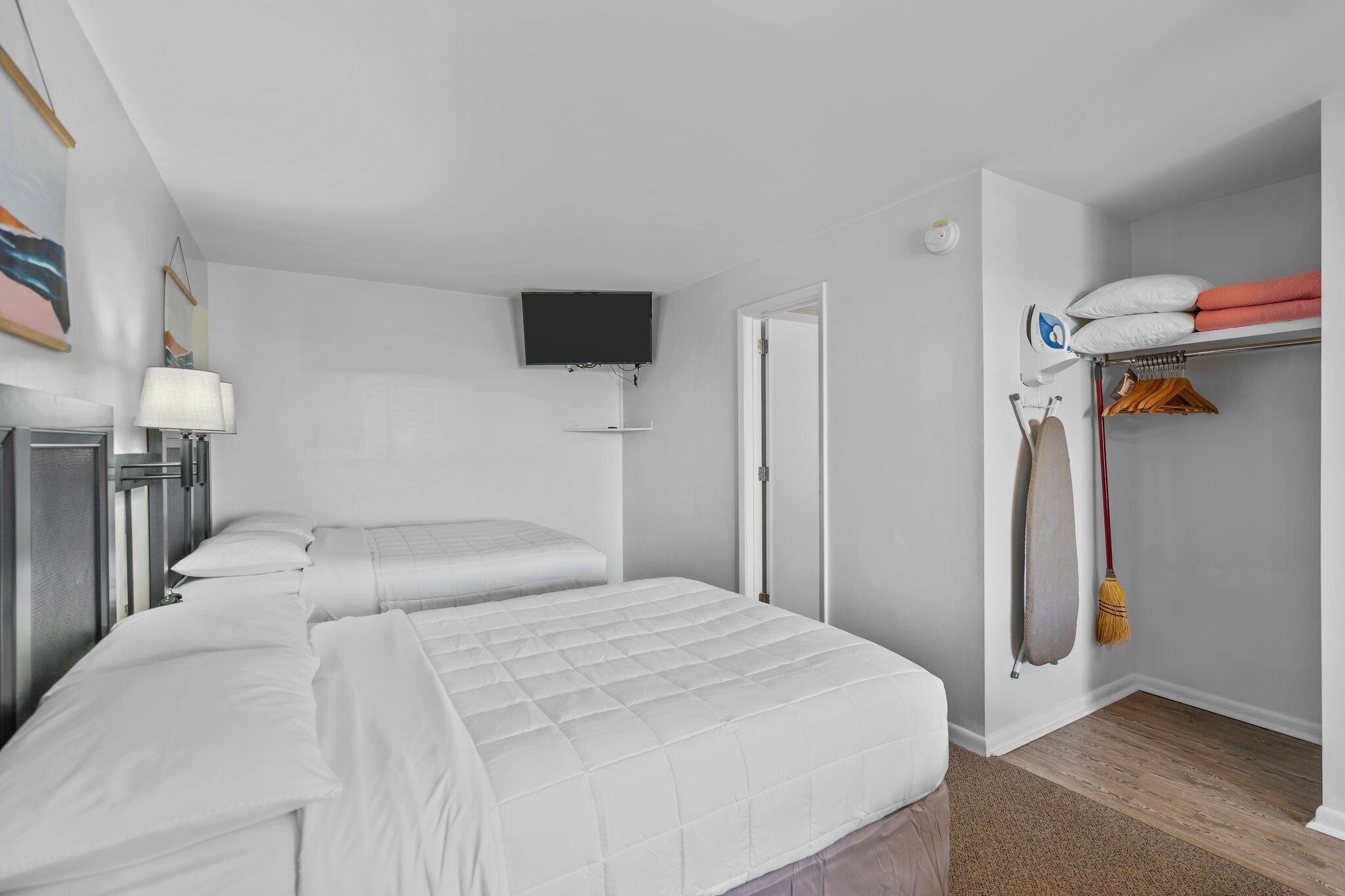 A hotel room with two beds, a TV mounted on the wall, a wardrobe, and a mirror.
