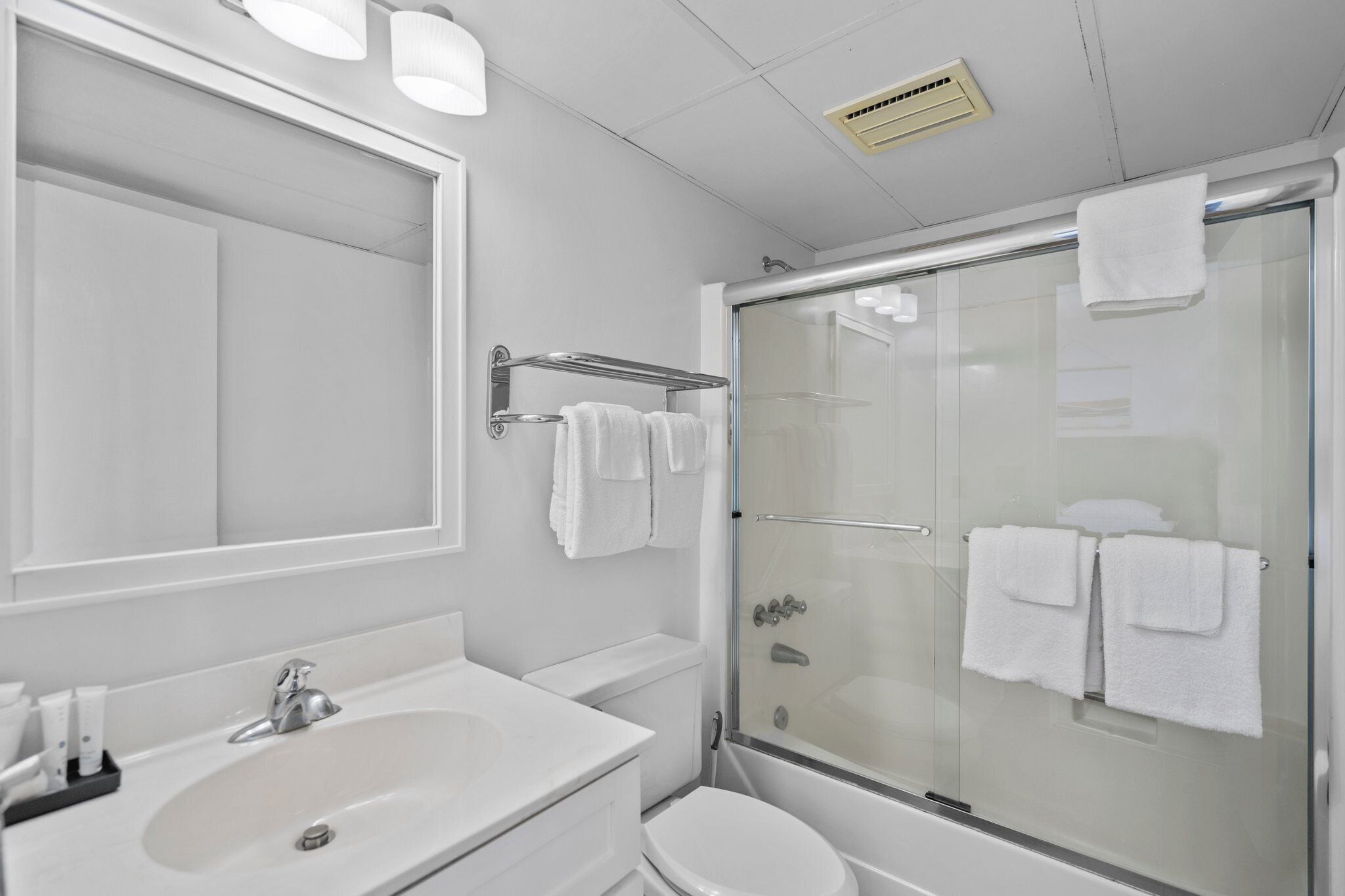 Un baño moderno con cabina de ducha de vidrio, un espejo grande y un lavamanos blanco.