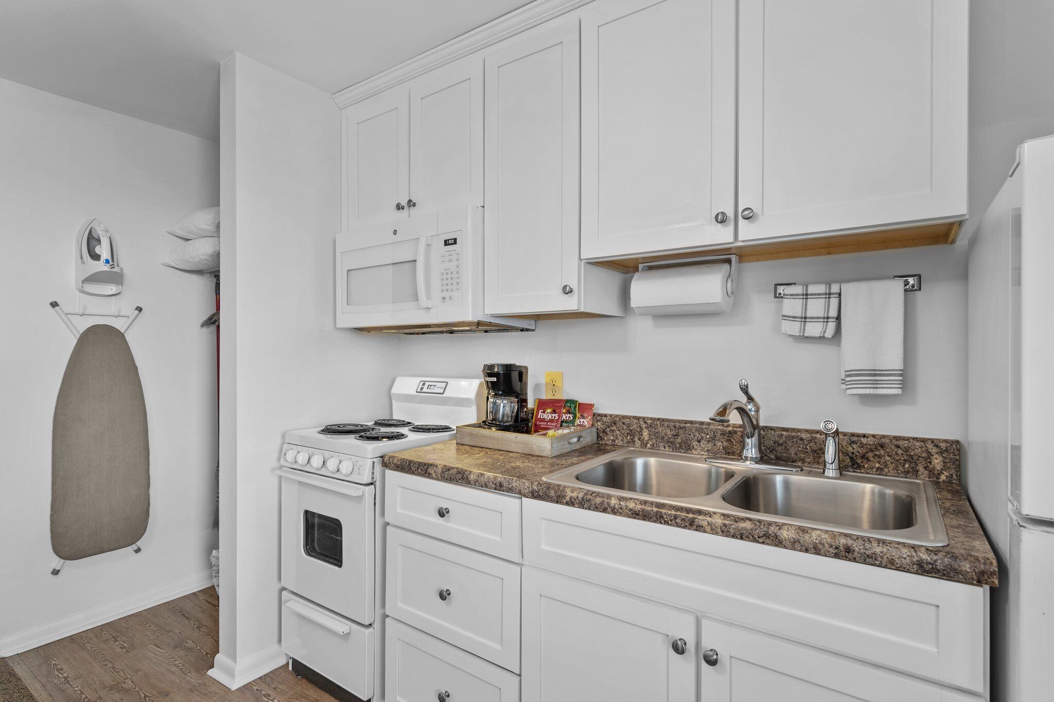 A kitchen with white cabinets, a stainless steel sink, a microwave, and a stove.