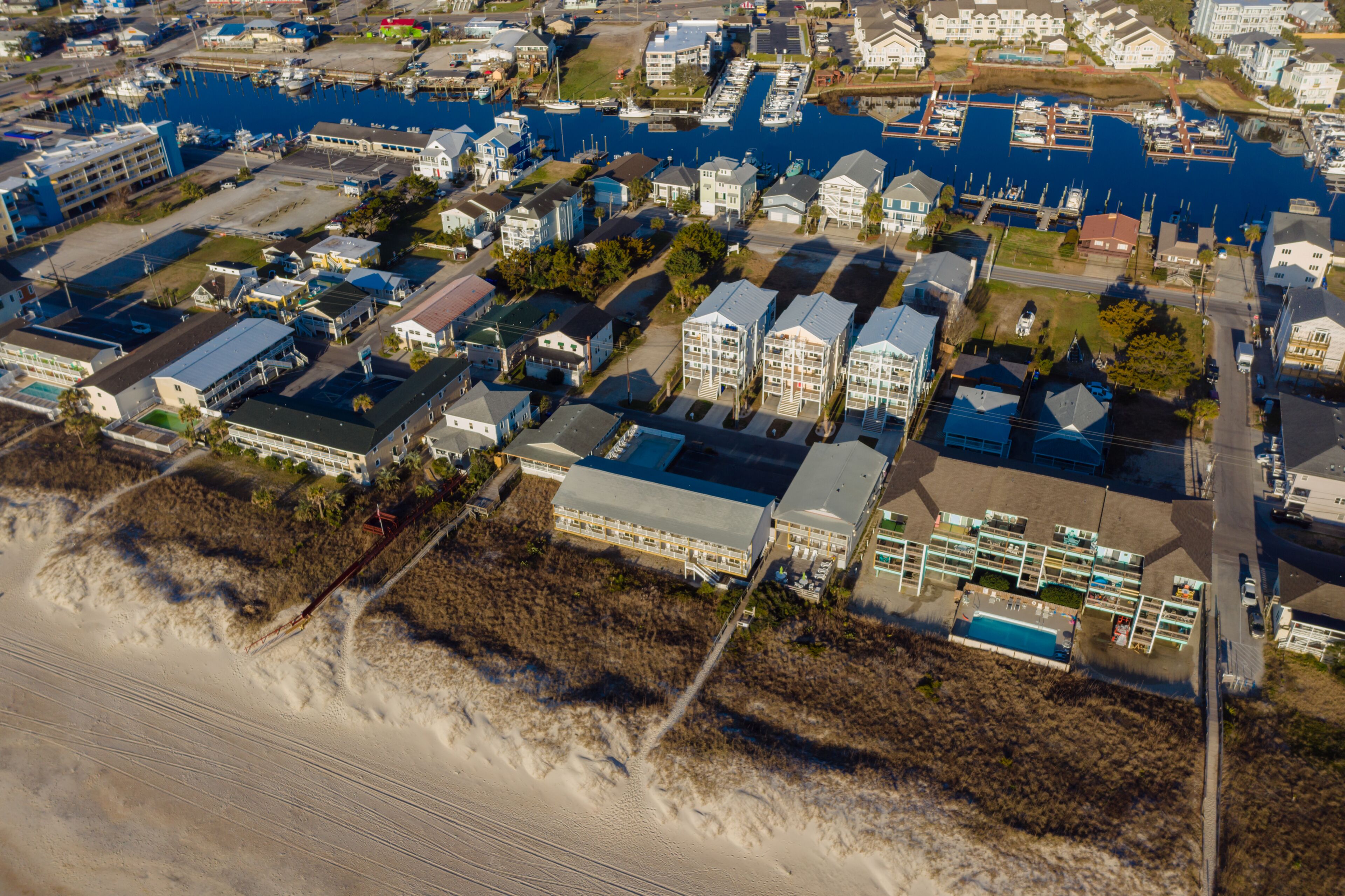 An aerial view of a coastal residential area with houses, a marina, and a beach.
