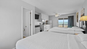 A hotel room with two beds, a kitchenette, and a balcony with a view of the ocean. - The Beach House (Carolina Beach)
