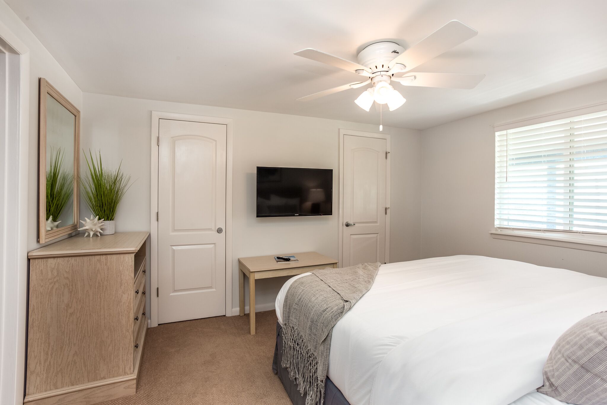 Une chambre à coucher comprenant un lit, un bureau, une télévision, une armoire et un ventilateur de plafond.