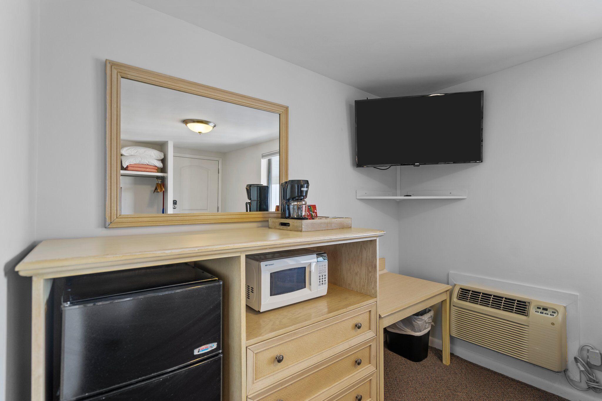 A compact hotel room with a wooden desk, a microwave, a refrigerator, a TV, and a heater.