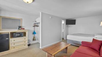 Een knus kamertje met een kitchenette, een bed, een rode bank, een houten bankje en een aan de muur bevestigde televisie.