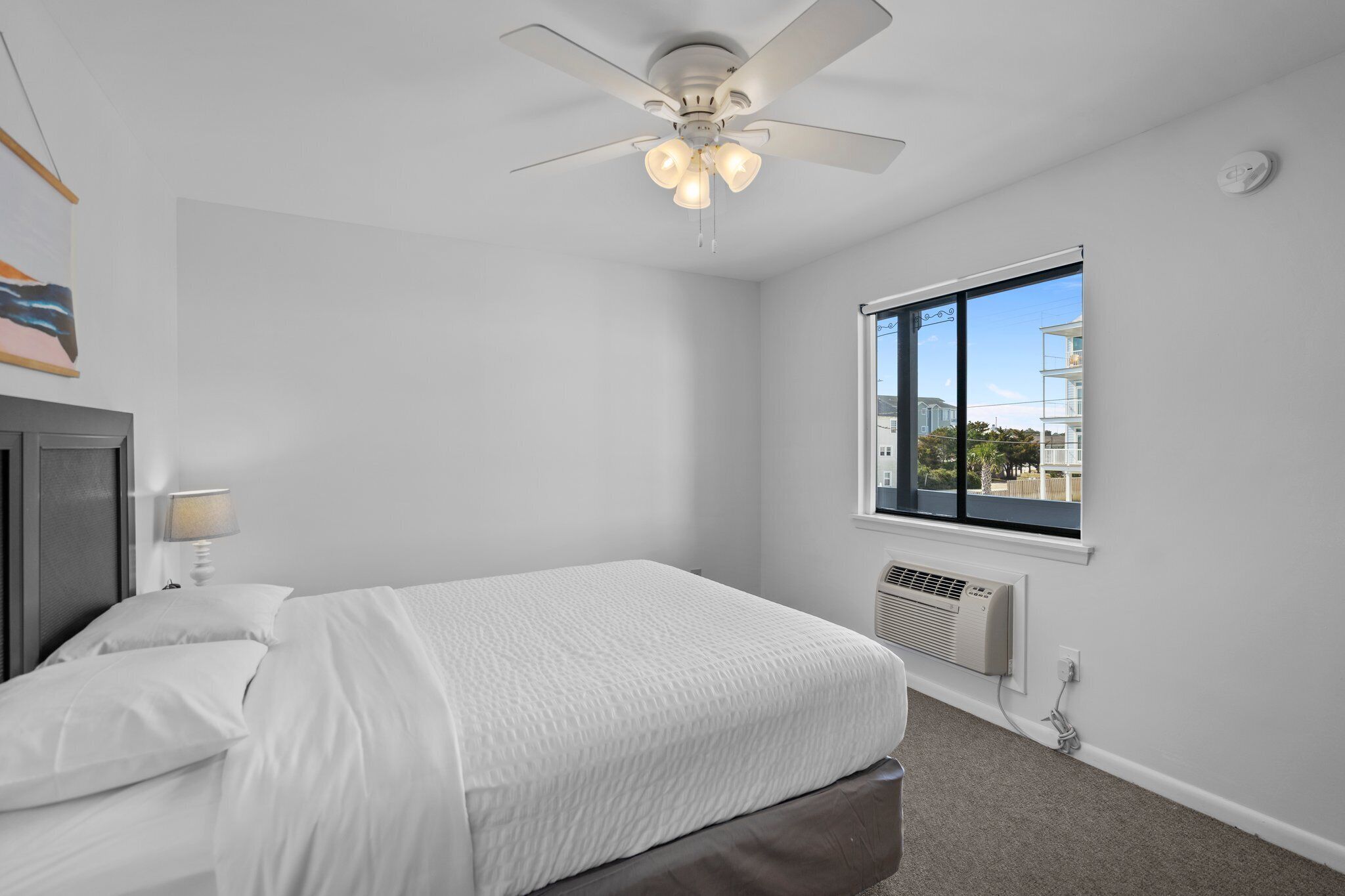 Quarto com cama, ventoinha no teto, janela com vista e aquecedor fixado na parede.