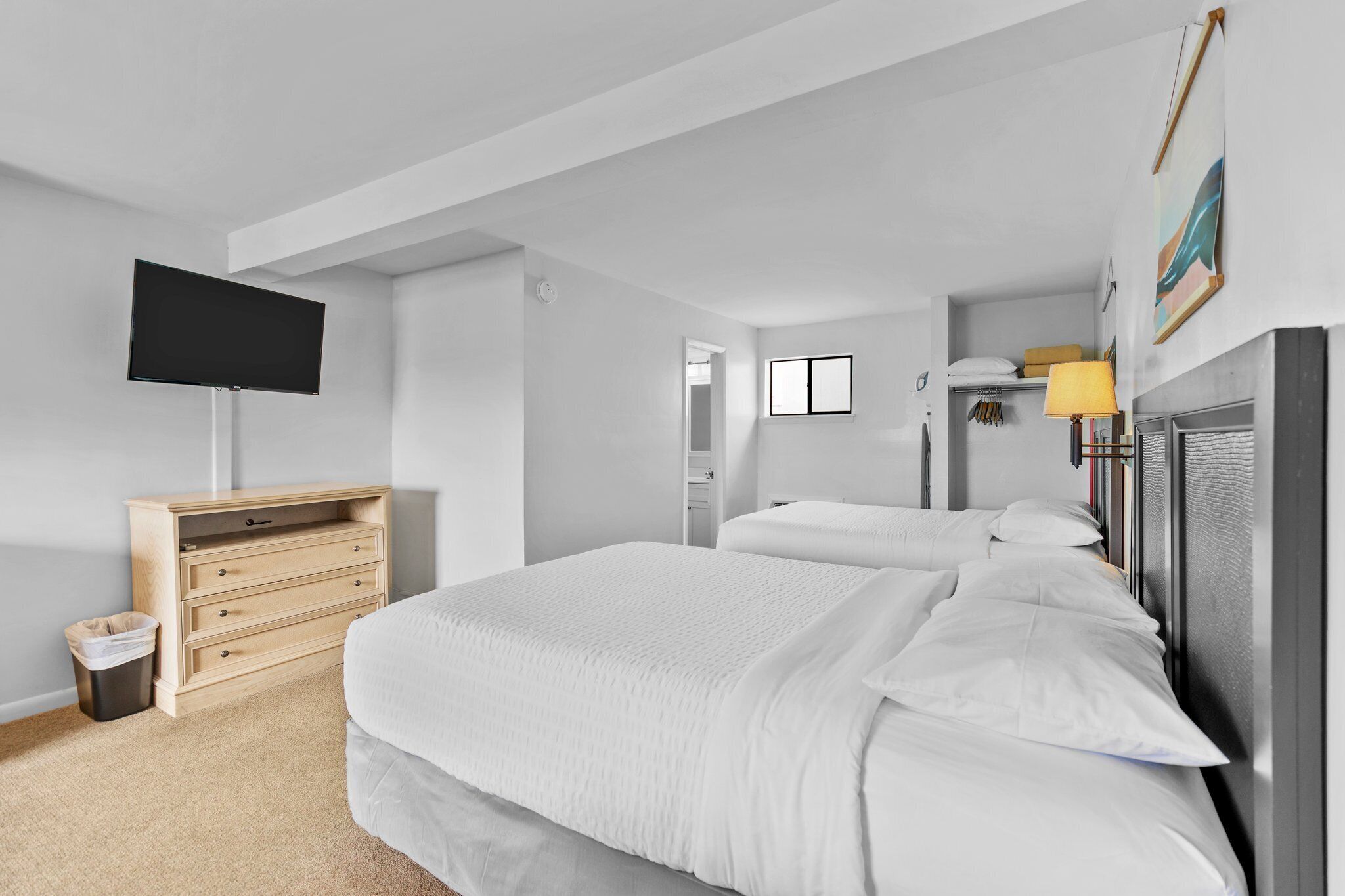 Un dormitorio con una cama grande, un televisor montado en la pared, un aparador de madera y un pequeño cubo de basura.