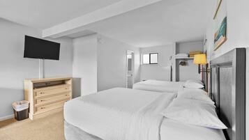 Een slaapkamer met een groot bed, een tv aan de muur, een houten dressoir en een kleine afvalbak.