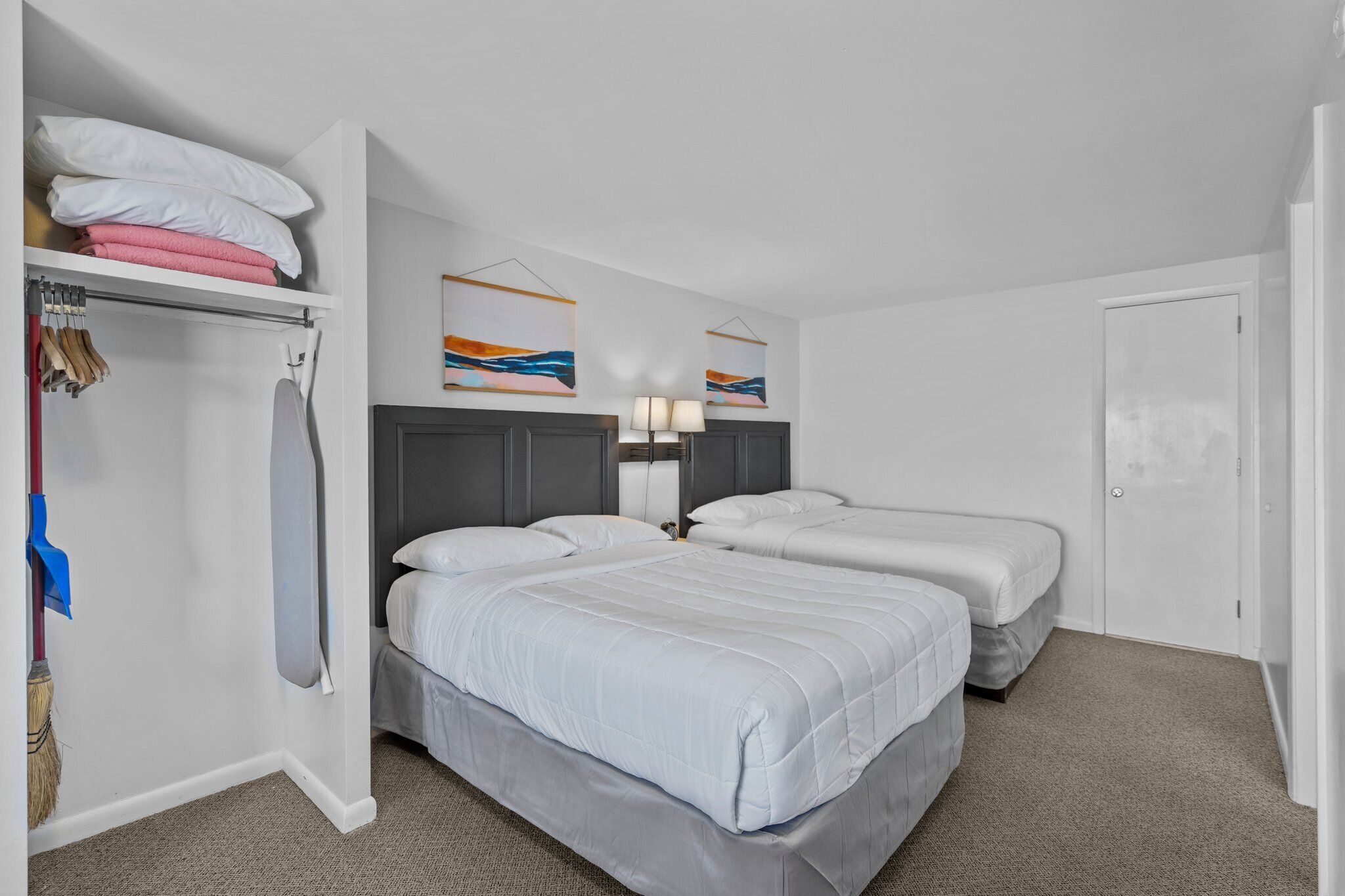 Habitación de hotel con dos camas, un armario y un cuadro en la pared.