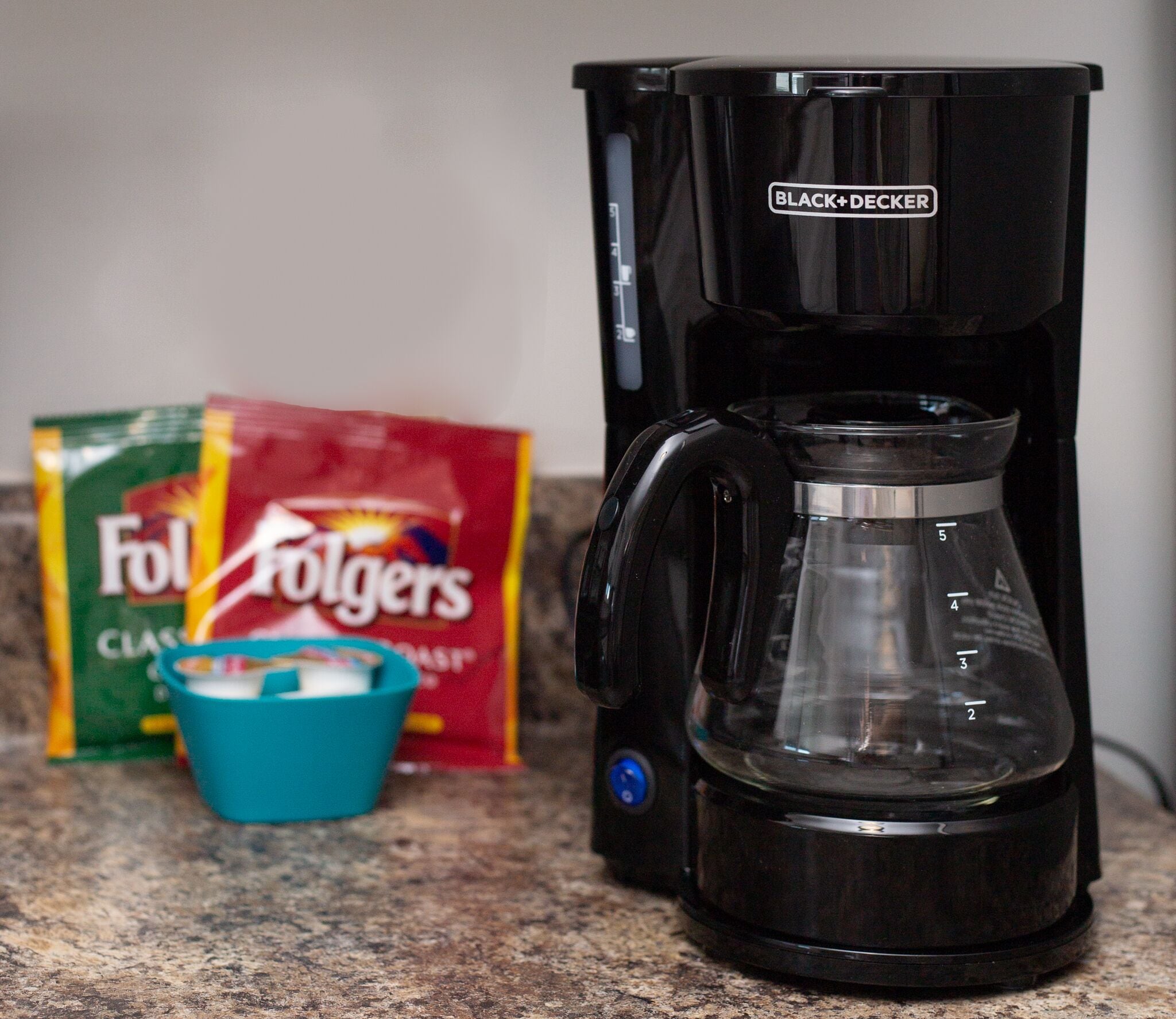 Een koffiezetapparaat, een zak Folgers koffie en een blauwe mok op een aanrecht.