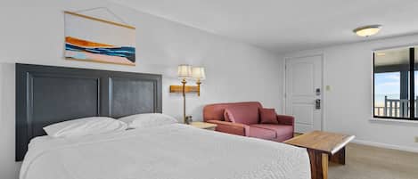 Una habitación de hotel con una cama grande, un escritorio, una silla, una lámpara y un cuadro en la pared.