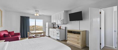 A hotel room with a large bed, a dining table, a kitchenette, a TV, and a balcony.